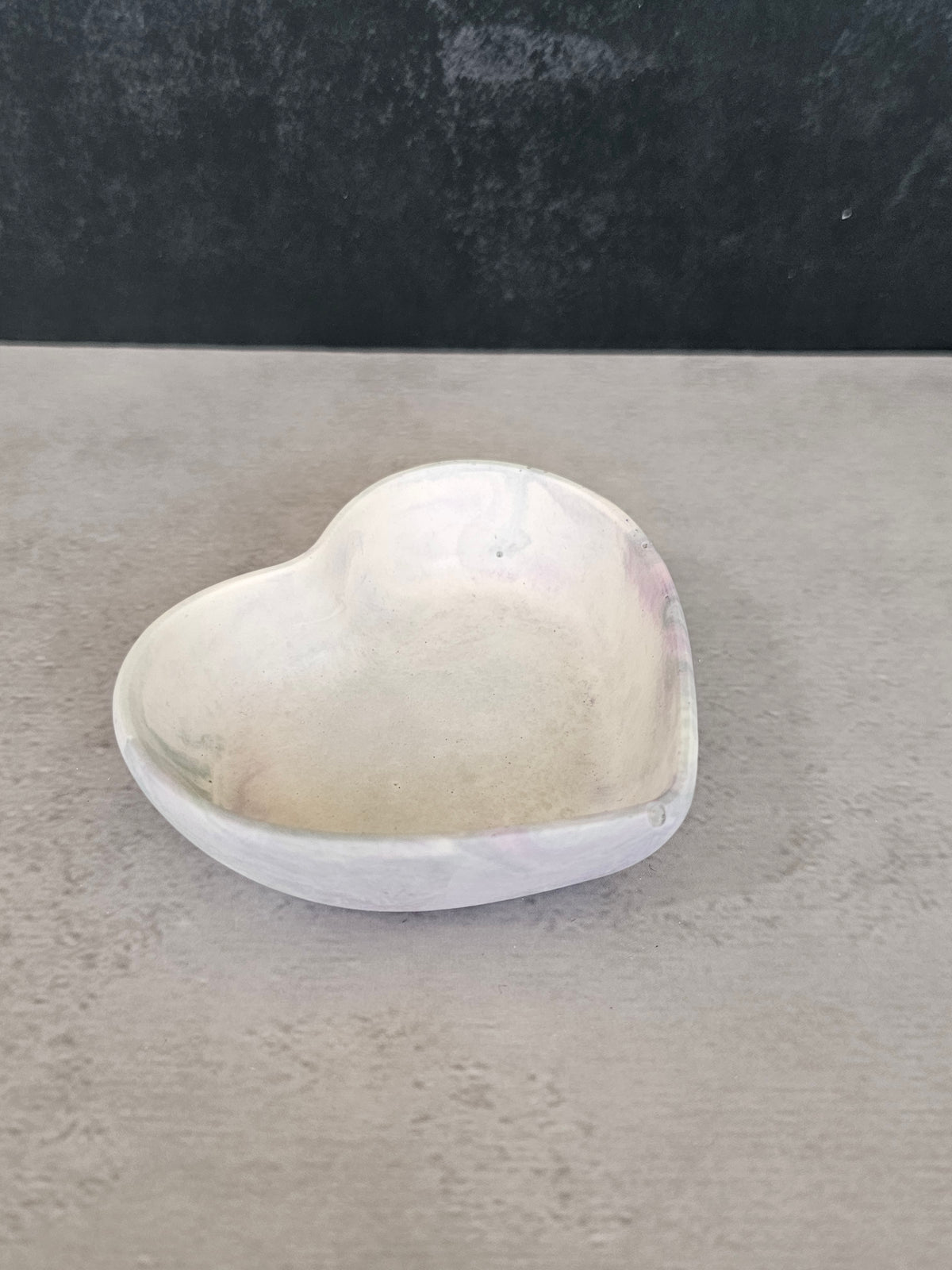 A small heart-shaped trinket bowl or dish, placed on a textured gray surface against a dark gray background.