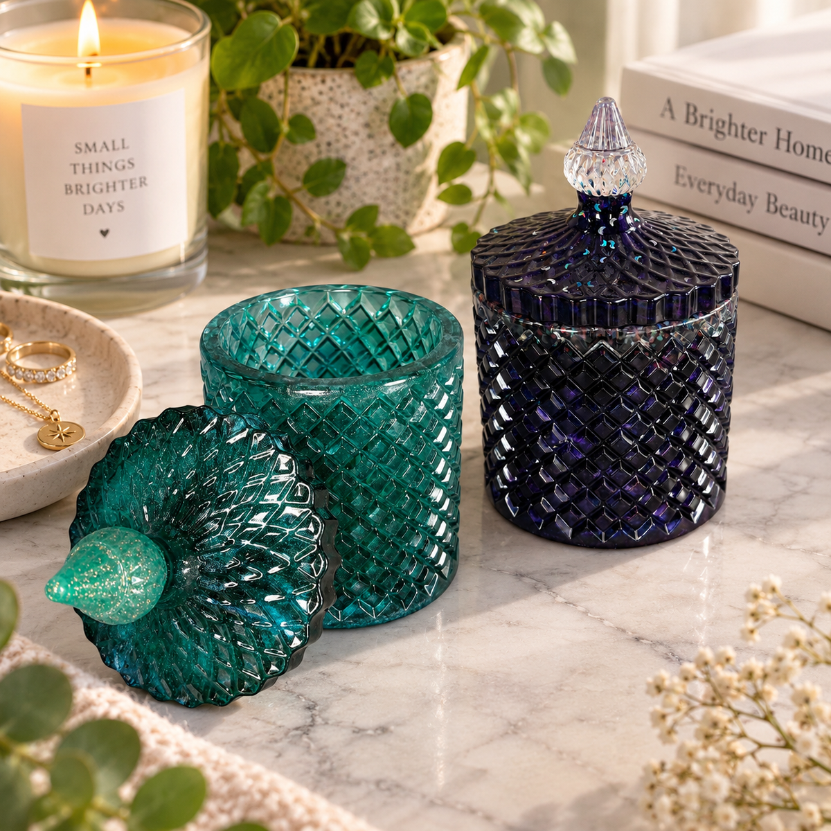 Two diamond-textured resin trinket jars on a marble tabletop. The Deep Teal jar is open with its decorative lid beside it, while the Midnight Shimmer jar is closed with a clear pointed handle.